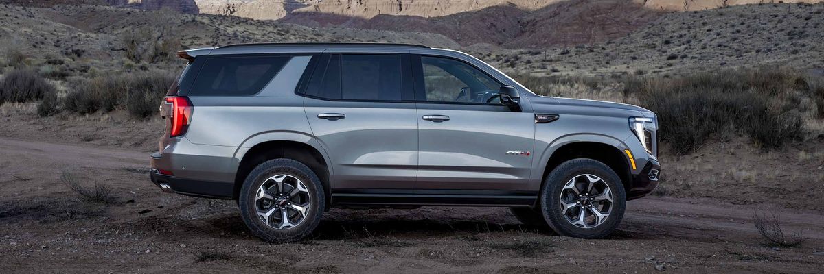 2026 GMC Yukon AT4 side profile parked on unpaved terrain with desert hills in background