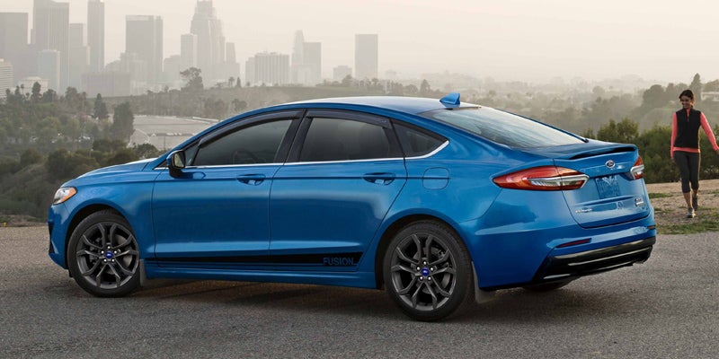 Blue 2020 Ford Fusion parked on an asphalt road with a blurred city skyline in the smoky background.