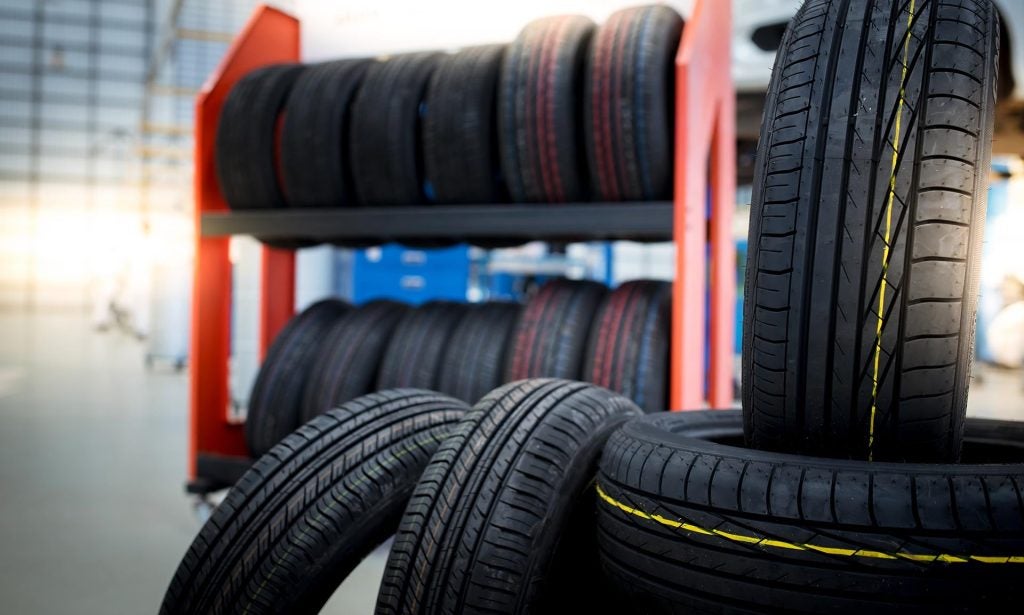Close-up of new tires stacked in a tire shop, with more tires on shelves in the background.