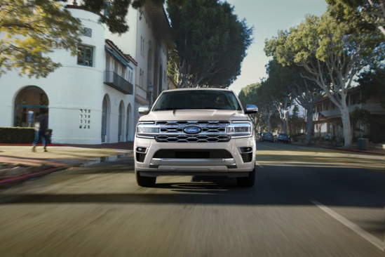 A White Ford Expedition SUV driving on a road between House.