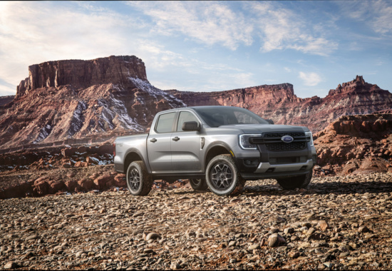 Silver Ford Ranger pickup truck with FX4 badging on a dirt path, kicked up dust behind it, with rocky hills in the background.
