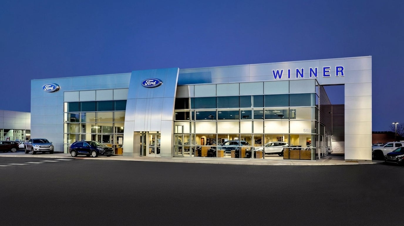 Exterior of modern Winner Ford car dealership building illuminated at dusk with cars parked around. (Representative image for illustration purposes only. Actual vehicle may vary based on trim and configuration.)