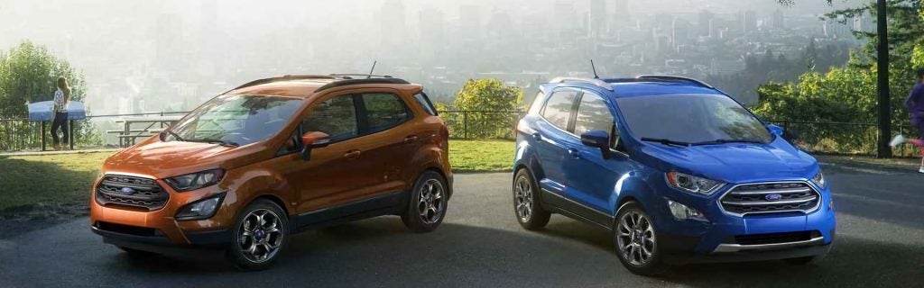 Two Ford EcoSport SUVs, one brown and one blue, parked outdoors with a city skyline in the background.