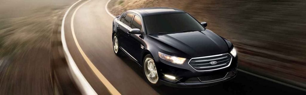 A shiny black Ford sedan driving quickly with motion blur on a winding road.