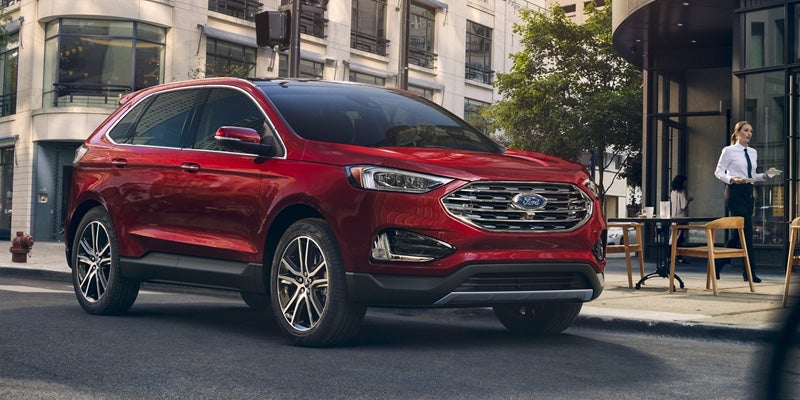 A shiny red Ford Edge SUV parked on a city street next to a cafe with outdoor seating and a waitress.