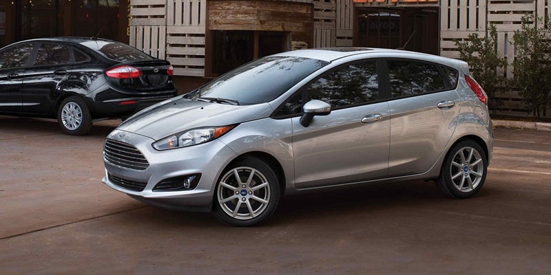 A silver Ford Fiesta hatchback parked diagonally in front of a dark Ford Fiesta sedan, both on a paved lot.