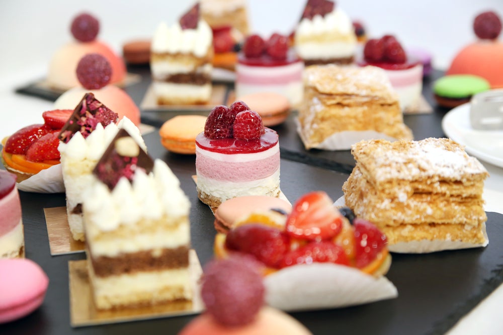 An array of colorful French pastries, including raspberry mousse cakes, strawberry tarts, macarons, and mille-feuille.