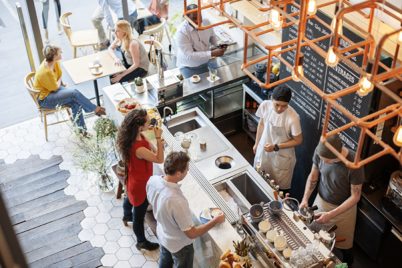 Overhead view of a bustling coffee shop with customers sitting at tables and ordering at the counter.