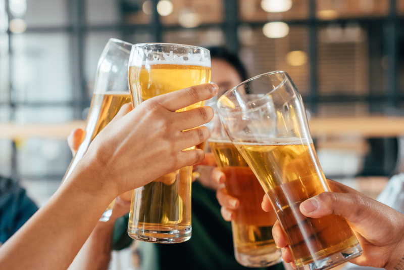Friends clinking glasses of beer together in a casual indoor setting.