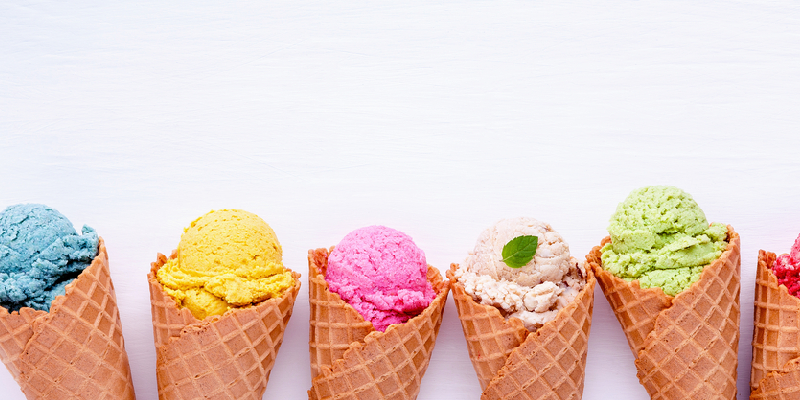Six colorful scoops of ice cream in waffle cones against a white background.
