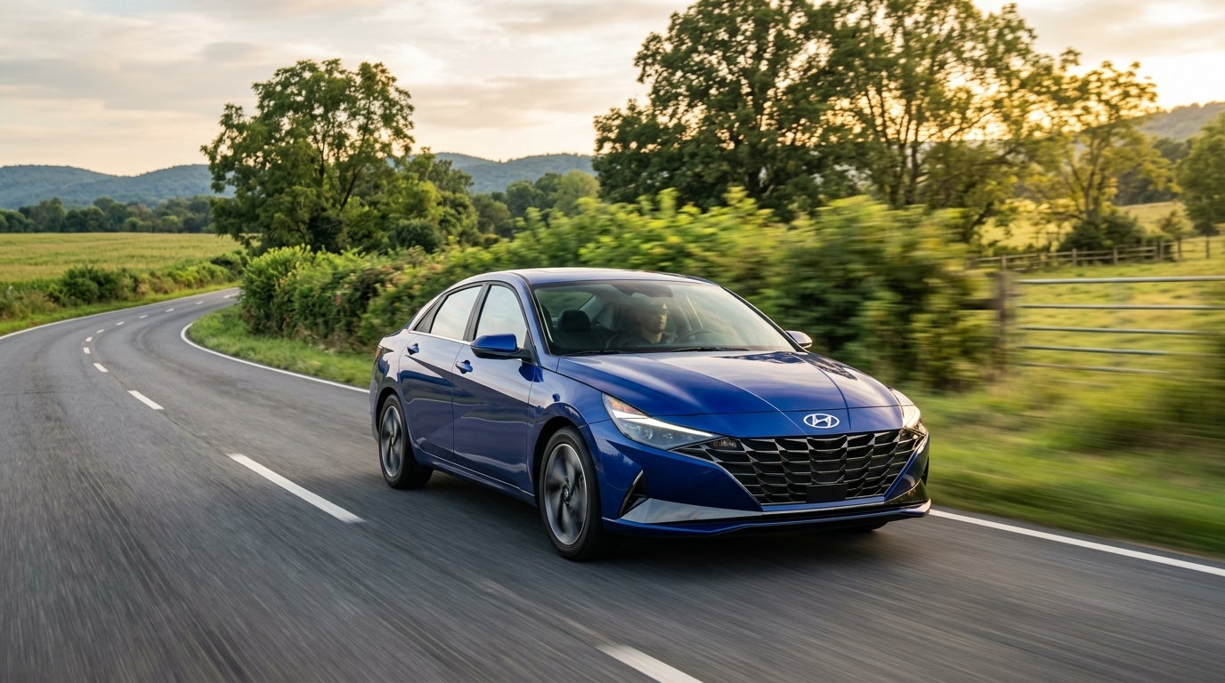 Blue Hyundai Elantra sedan driving along a winding country road flanked by green fields and trees at sunset. (Representative image for illustration purposes only. Actual vehicle may vary based on trim and configuration.)