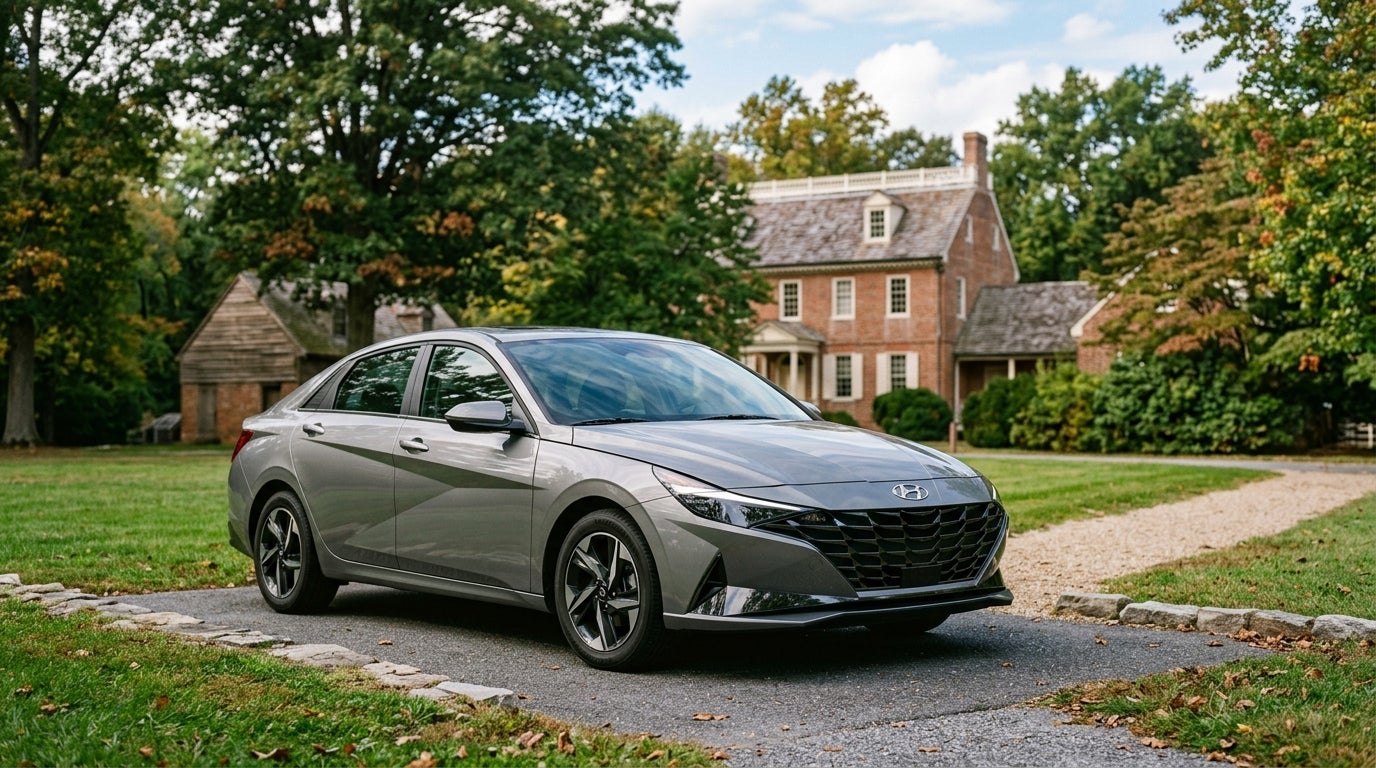 A gray Hyundai Elantra parked on a paved driveway in front of a historic brick colonial house. (Representative image for illustration purposes only. Actual vehicle may vary based on trim and configuration.)