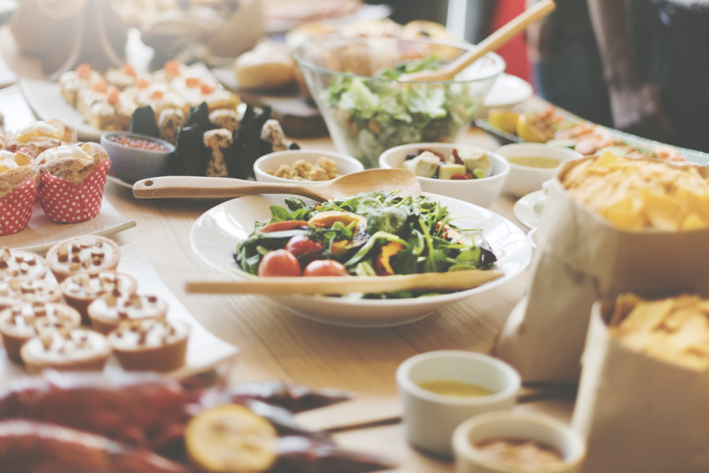 A buffet table laden with diverse dishes including salads, pastries, chips, tarts, and other appetizers.