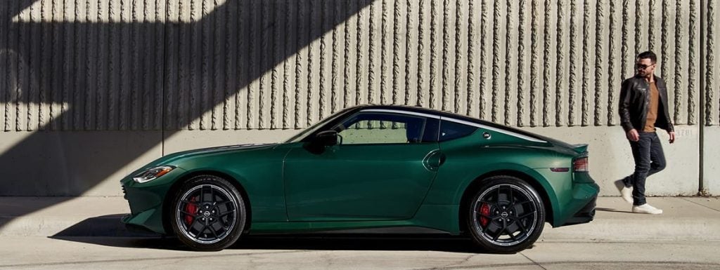 Green Nissan Z sports coupe parked beside a concrete wall, showcasing its sleek profile while a person stands nearby.