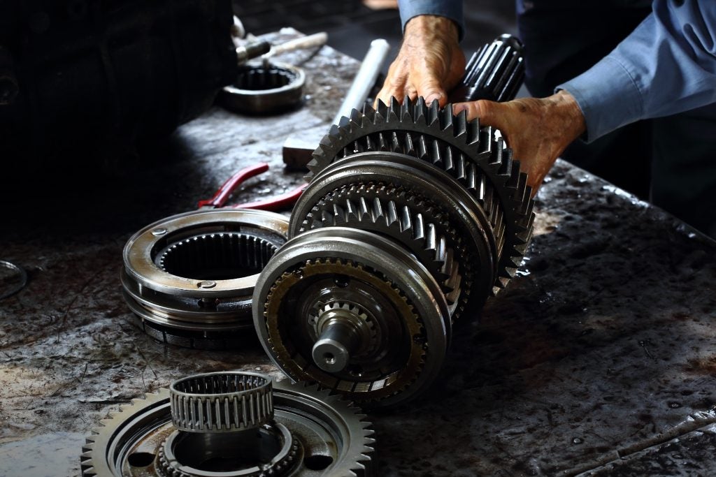 A mechanic assembling a complex transmission gear shaft assembly on a grease-covered workbench.