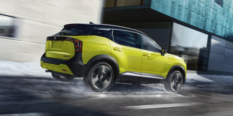 A bright yellow Nissan Kicks crossover SUV driving on a wet, slushy street next to modern buildings.