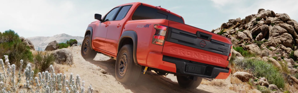 Red Nissan Frontier PRO-4X tackling a rocky off-road trail in a desert landscape