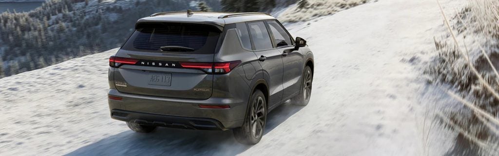A dark gray Nissan Rogue Platinum SUV driving down a snow-covered road.