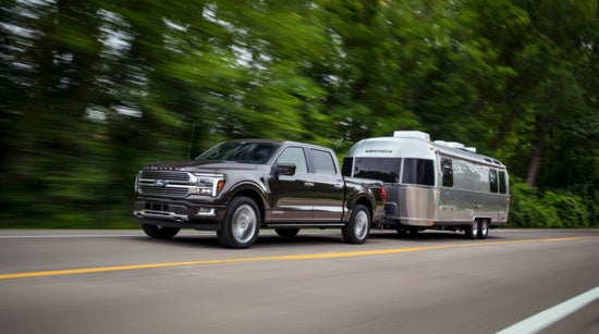 A silver Ford pickup truck towing a sleek silver Airstream trailer on a forested road