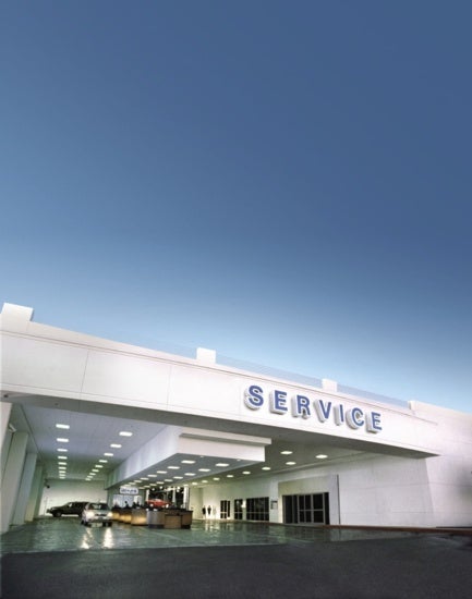 White modern automotive service center with "SERVICE" sign, cars inside brightly lit service bay under clear blue sky