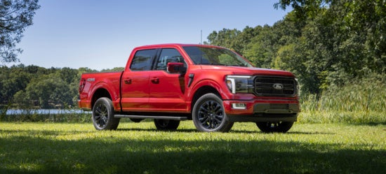 Bright red Ford F-150 pickup truck parked on grass with trees and water in background, modern rugged design