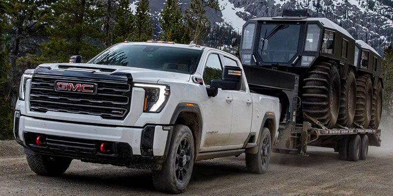 White GMC Sierra towing heavy off-road vehicle on a dirt mountain road.