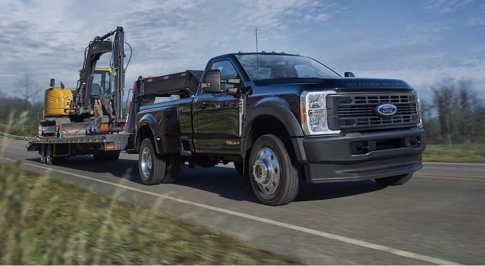 A black 2025 Ford F-450 towing heavy machinery.