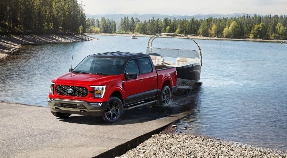 A red 2024 Ford F-150 XLT Heritage Edition towing a boat out of a lake