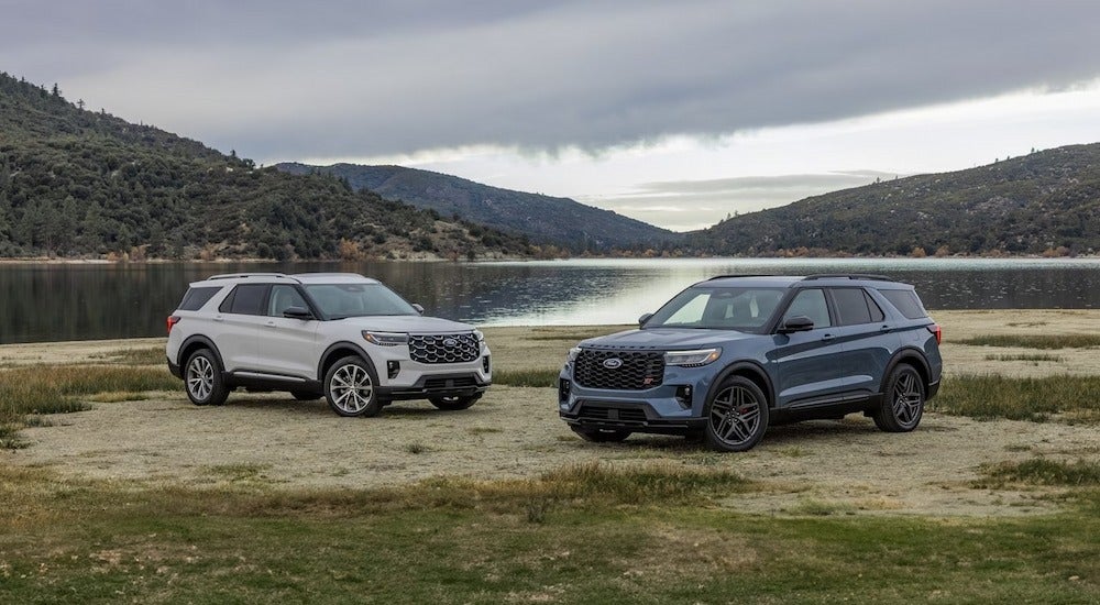 A white 2025 Ford Explorer Platinum and a blue 2025 Explorer ST parked at a lake
