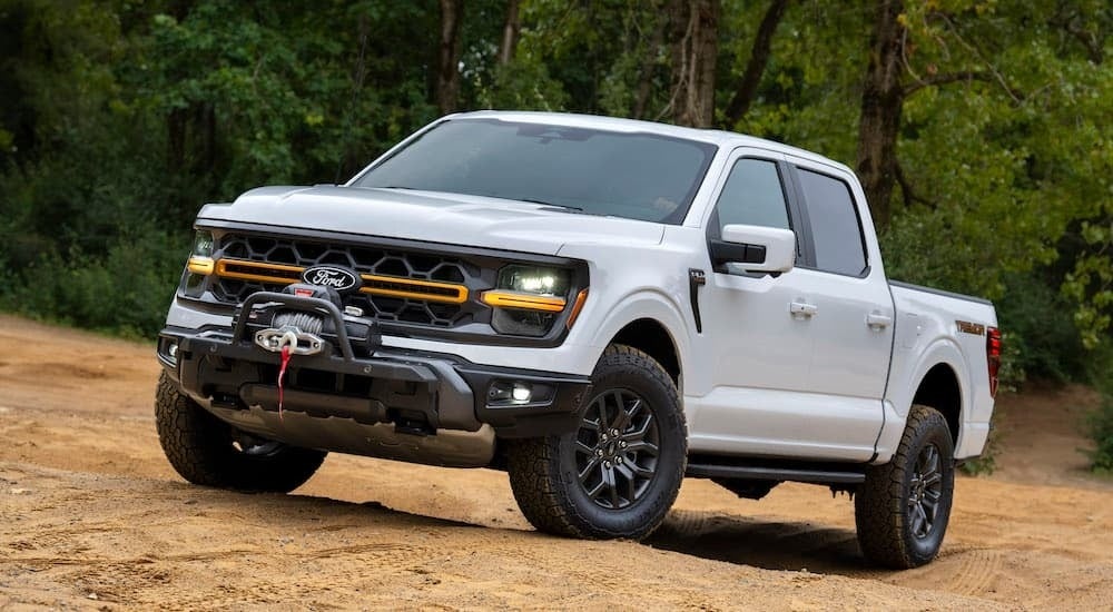 A white 2024 Ford F-150 Tremor is shown from the front at an angle while parked off-road after leaving a dealer that has a Ford trucks for sale