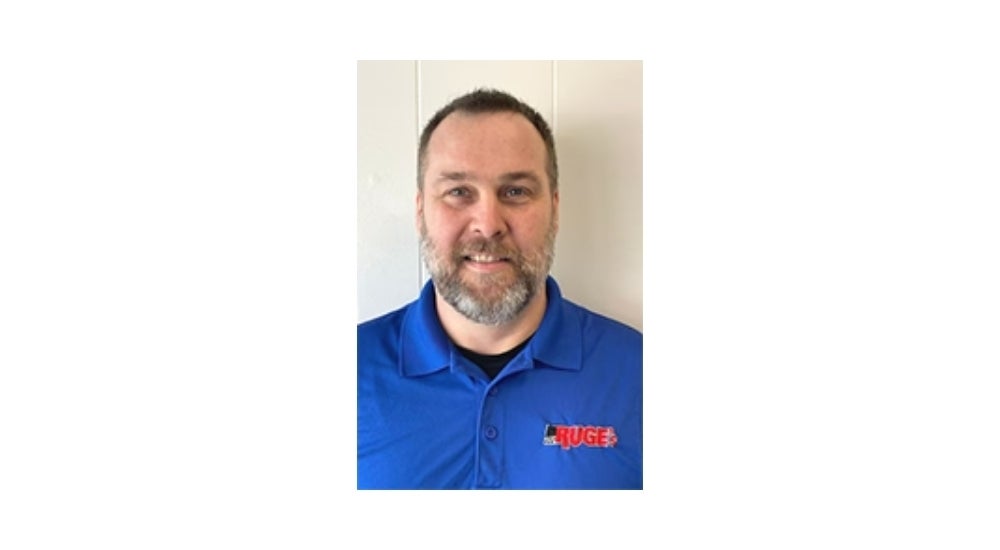 Alt text: Middle-aged man in blue Kuge polo shirt, smiling with gray beard, standing against white background