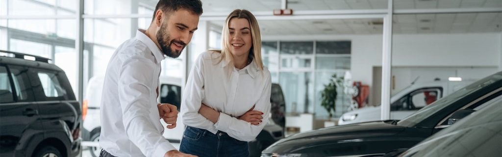 Customers exploring vehicles at Caughlin Buick GMC Newark showroom with a sales representative discussing car features.