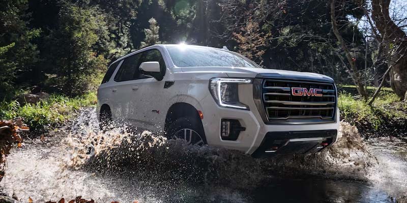 brand new white 2023 GMC Yukon trudging through a body of water having off road fun