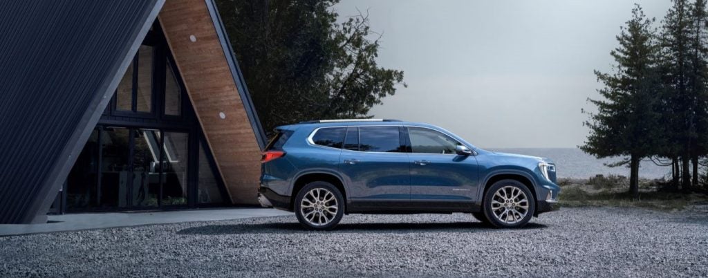 Blue 2024 GMC Acadia Denali parked near a cabin