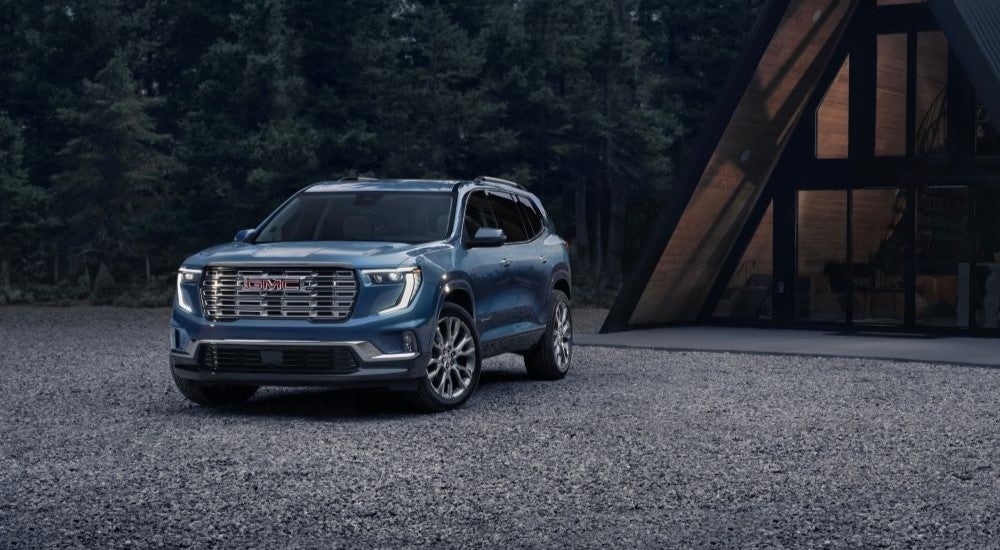 Blue 2024 GMC Acadia Denali parked in front of a cabin