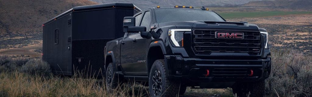 2026 GMC Sierra 2500 HD AT4X towing a trailer in an off-road landscape, highlighting powerful towing capability and heavy-duty performance.
