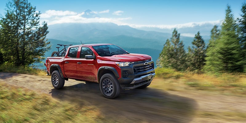 Red Chevrolet Colorado pickup truck driving down a dirt path with a mountain bike in the bed.