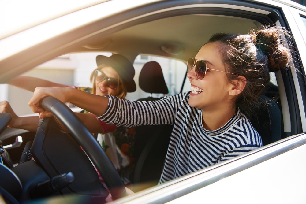 2 laughing women are sitting in the front seat of a GMC SUV enjoying their ride