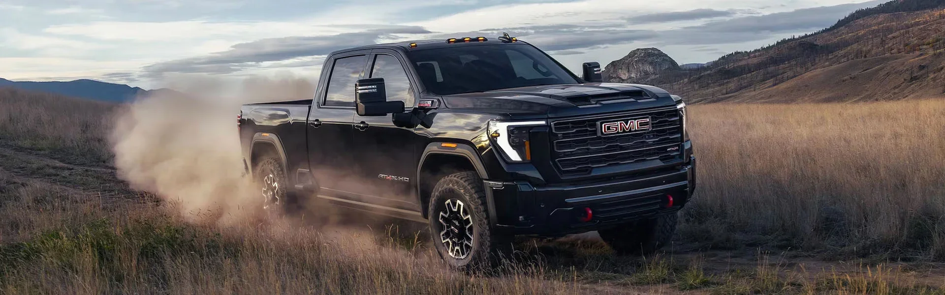 A black GMC Sierra 2500 driving trhough a dusty field