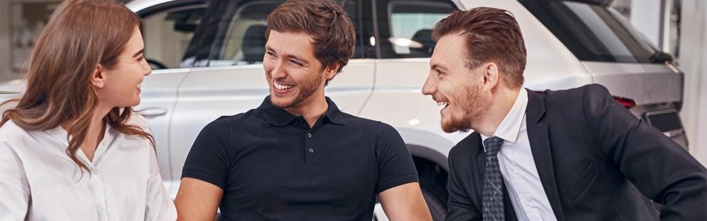 A couple and GMC salesman all smiling together as they talk about the white GMC SUV behind them