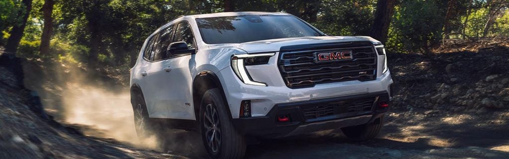 2026 GMC Acadia AT4 SUV driving on a rugged forest trail, showcasing bold front styling, LED lighting, off-road capability, and premium SUV design at Country Club GMC in Oneonta, NY.