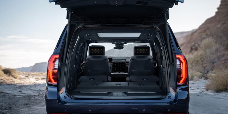 Maximum Space and Comfort is being shown through the open trunk door of a black GMC Yukon SUV sitting in the sand at a hilly beach.