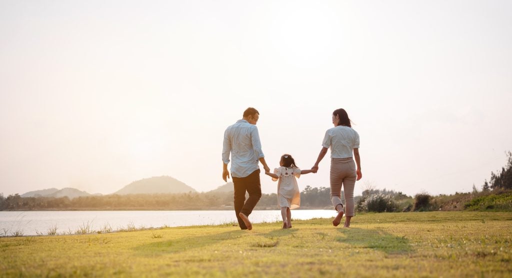 Parents holding their child's hands while walking outdoors.