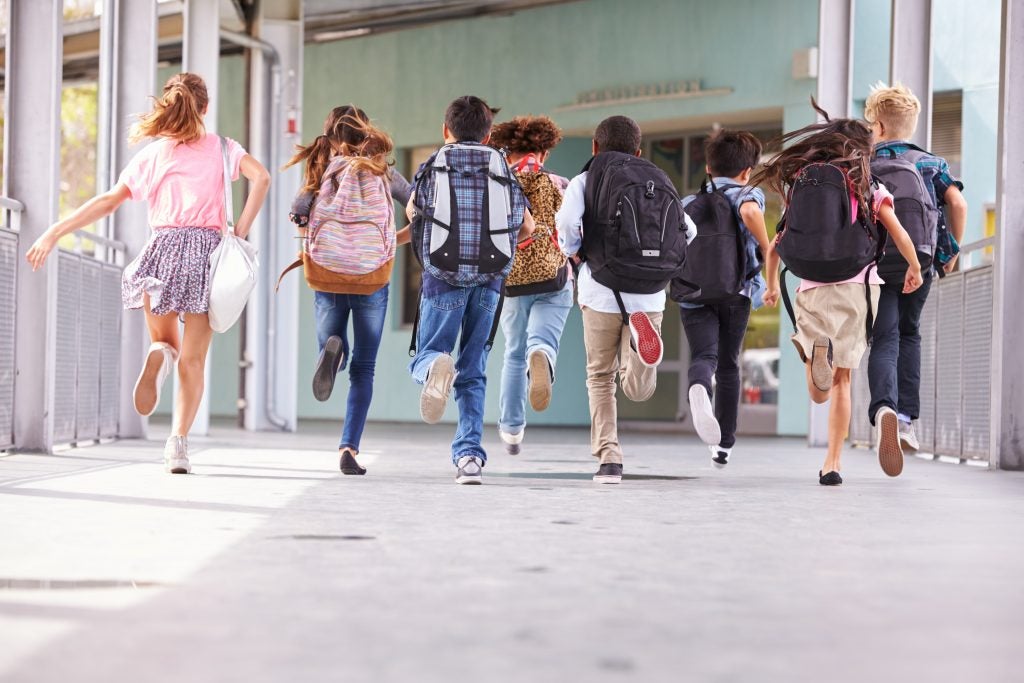 Kids running together outside a school building.