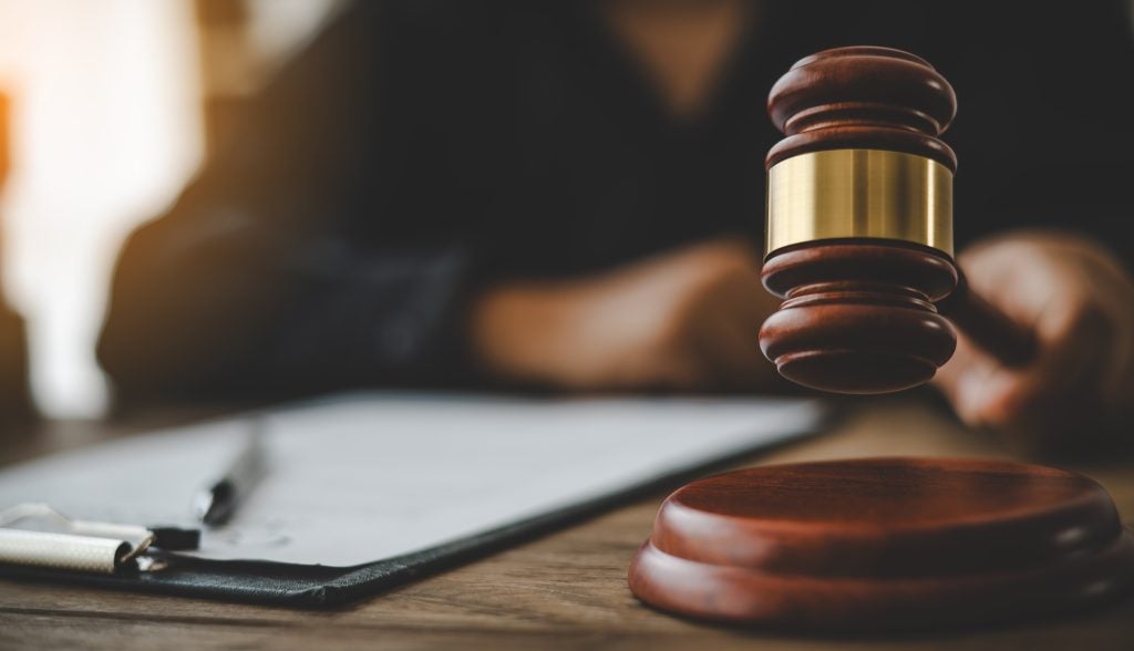A lawyer's hand firmly holds a gavel on a wooden table.