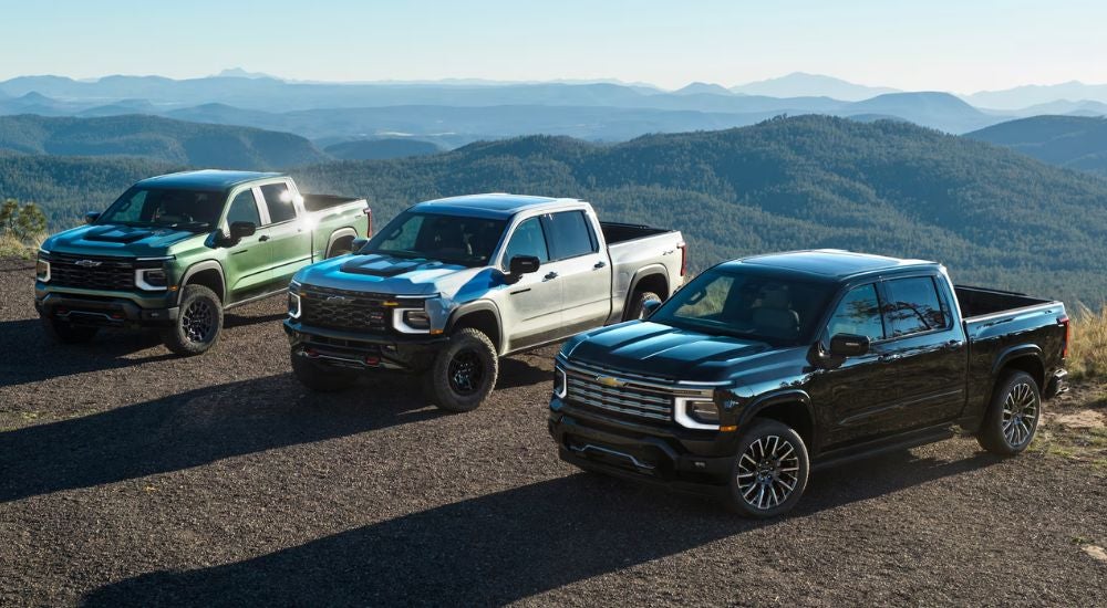 A trio of 2027 Chevy Silverado 1500s in green, white and black with mountains in the background.