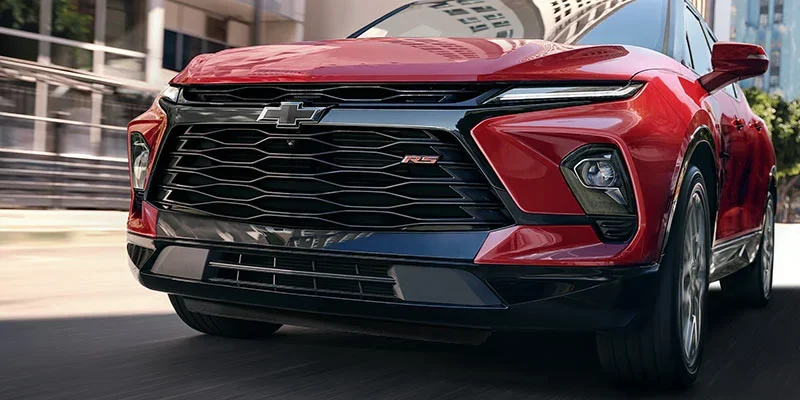A close-up of a red Chevrolet Blazer RS driving through a city street, showcasing its bold front grille and sleek design.