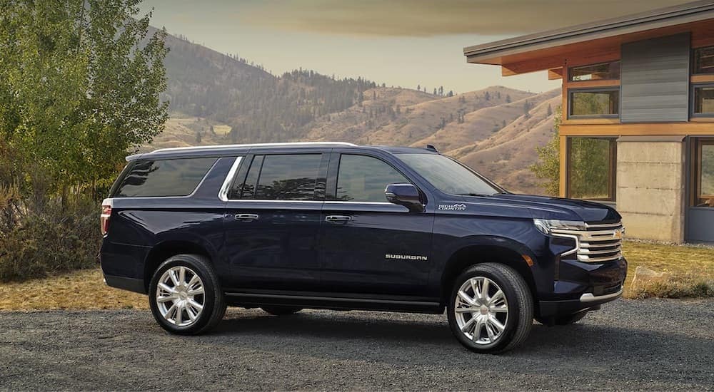 A dark blue 2024 Chevy Suburban High Country is shown parked outside a house.