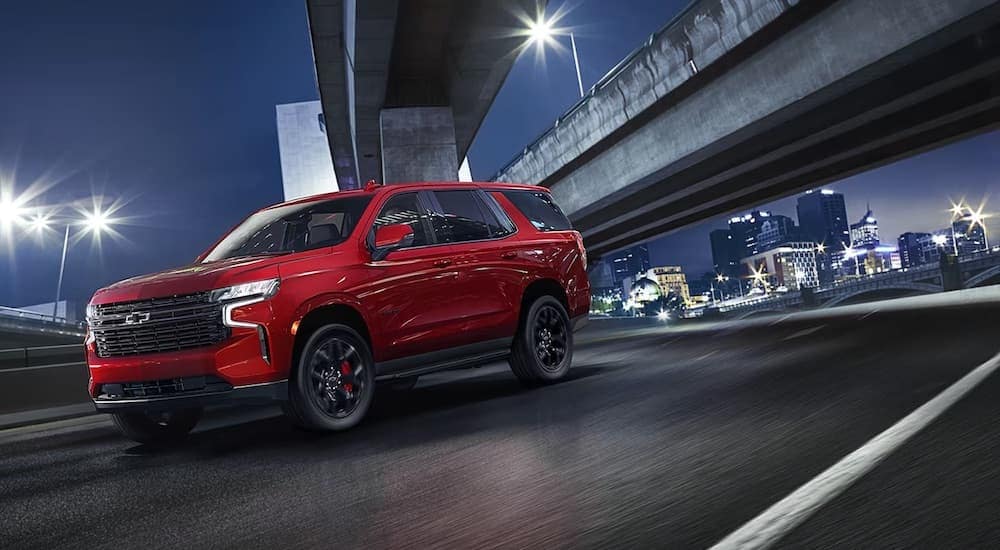 A red 2024 Chevy Tahoe RST is shown driving in a city.