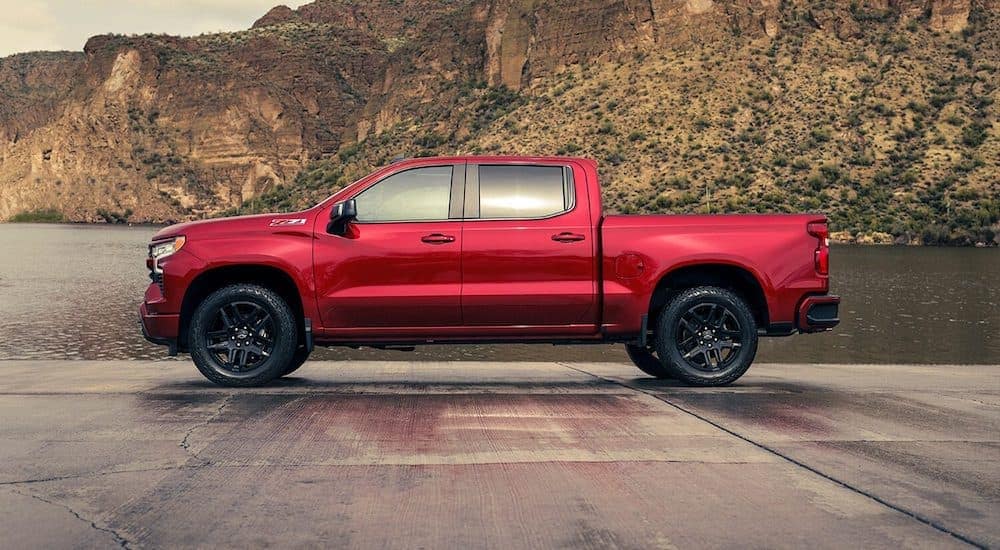 a red chevy truck sits parked on concrete with rocky hills and water in the background 